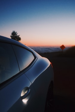 A sleek luxury car parked on a scenic coastal road during sunset.