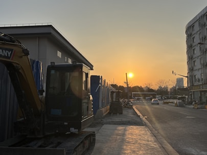 Modern construction machinery quietly parked at a building site during sunset.