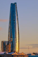 A panoramic view of a commercial tower with reflective glass façade panels at sunset.