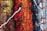 A close-up view of woven textiles featuring a variety of vibrant colors and textures. The arrangement includes sections of brown, green, red, black, and white fabrics, intricately interwoven with visible threads and fibers, including a prominent white thread crossing horizontally.