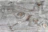 A textured wooden surface with visible grain patterns and knot holes. The wood shows natural variations and weathering, giving it a rustic and aged appearance.