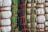A close-up view of intricately woven fabric patterns featuring a combination of threads in green, beige, and black colors. Thick brown ropes are used to bind sections of the textured fabric, creating an organized yet varied pattern with a distinct tactile quality.