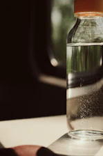 A clear glass of water with droplets on the bottle, set against a soft blue background symbolizing freshness and purity.