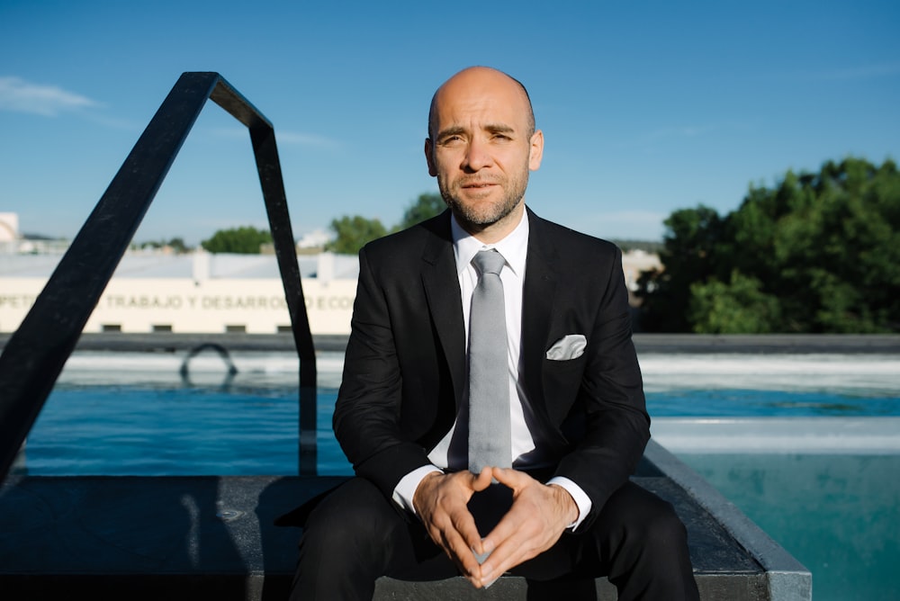 a man in a suit and tie sitting in front of a pool