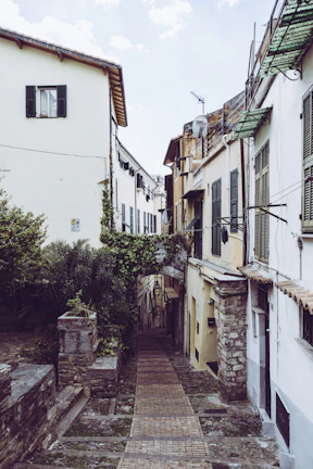 A quiet cobblestone alleyway lined with charming old buildings and flowering balconies.