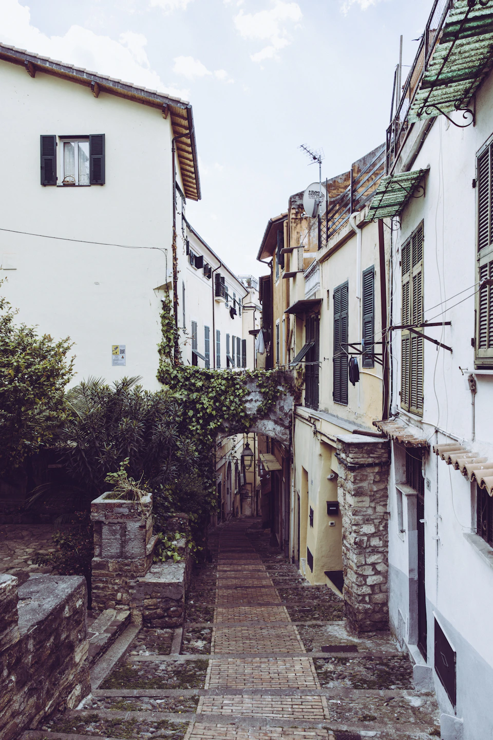 Narrow alleyway flanked by white buildings with stone wall and brick walkway upstairs
