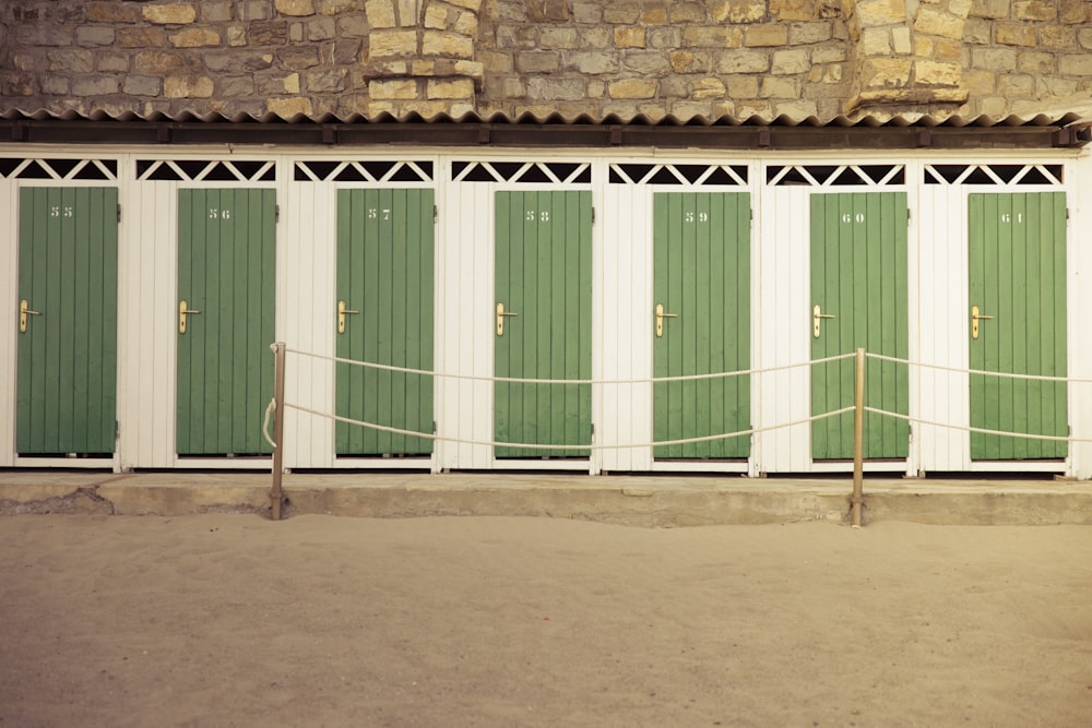 Una hilera de puertas verdes y blancas junto a una pared de ladrillo