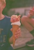 A child excitedly holding a double scoop cone with sprinkles and a cherry on top.