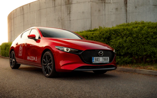 Close-up of a shiny red Mazda 3, highlighting its dynamic front grille and headlights.