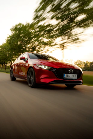 Mazda CX-8 driving on a scenic road with green trees on both sides, showcasing its stylish profile.