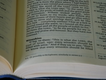 A close-up view of an open book displaying printed text in two columns, with a particular focus on the words 'Wineskins' and a passage discussing the commands of the Lord. The pages are slightly curved, indicating the book is either new or gently opened. The light casts a soft shadow, adding depth to the image.