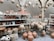 A collection of handcrafted pottery displayed on shelves and stands, including various shapes and sizes of pots, vases, and jugs. Hanging from arches are intricately designed lanterns. The setting has a rustic and traditional feel, with earthy tones and craftsman-style pillars.