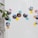 A refrigerator door is decorated with circular travel photos and colorful sticky notes. The images depict scenes from various locations, while the notes label each place with handwritten text. A green potted plant partially frames the left side of the image.