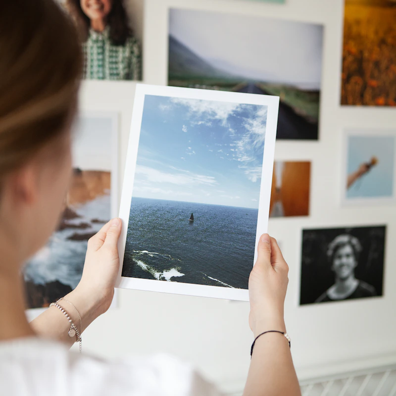 Hand holding a printed photo in front of a wall of photo prints - the kind of keepsake save-the-date magnets become