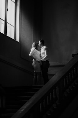 a black and white photo of a couple kissing on the stairs