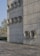 A modern architectural wall made of concrete panels featuring multiple circular protrusions arranged in a grid pattern. The smooth, industrial design gives it a minimalist aesthetic. A car is parked to the left, and trees are visible in the background, indicating an urban setting. The ground is paved with patterned stone tiles.