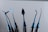 A set of six shiny blue metal instruments with various shaped ends, displayed vertically against a plain background. Each tool has a unique, intricate design, suggesting they are specialized for specific tasks.