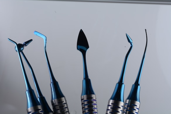 A set of six shiny blue metal instruments with various shaped ends, displayed vertically against a plain background. Each tool has a unique, intricate design, suggesting they are specialized for specific tasks.
