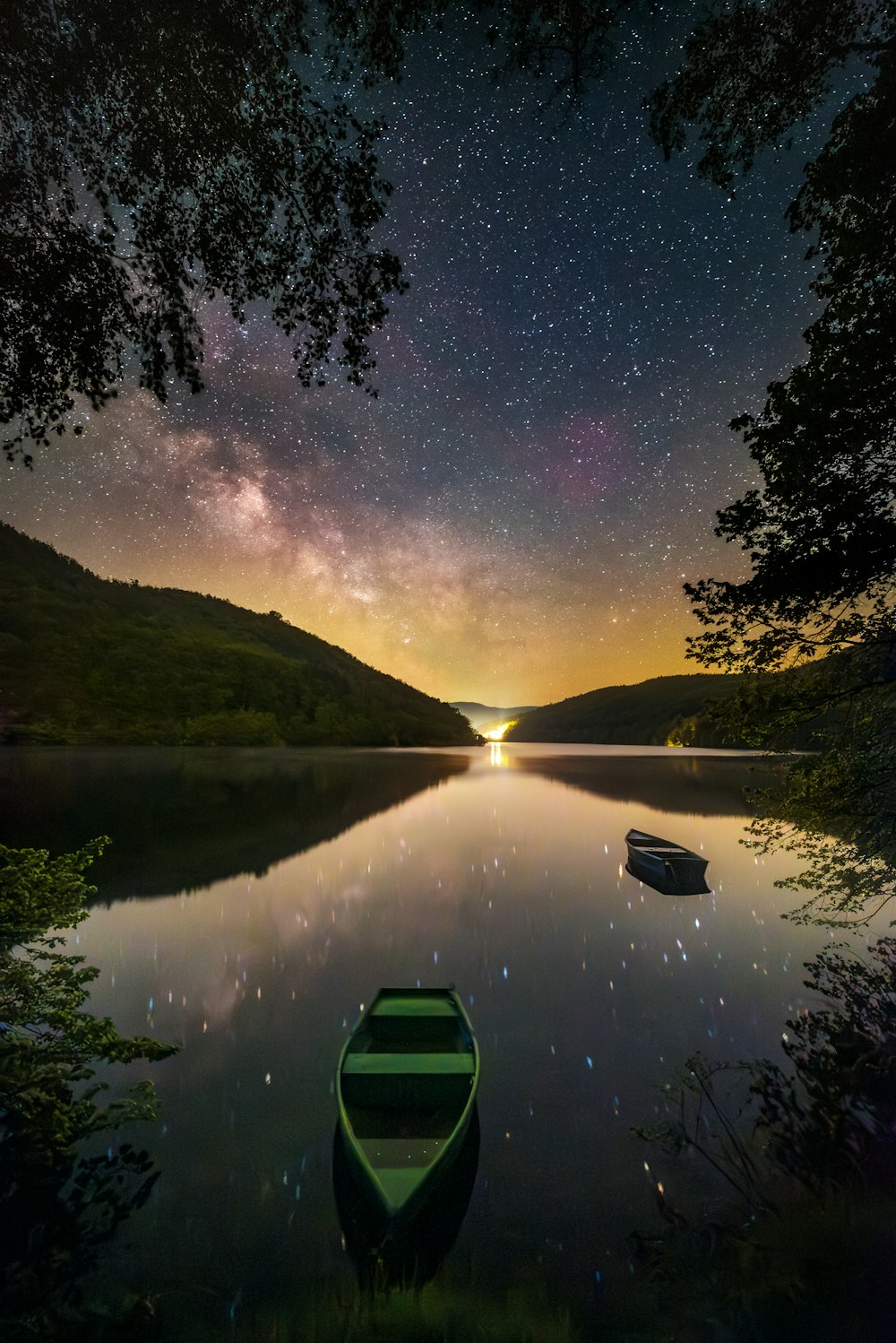 a green boat sitting on top of a lake under a night sky