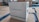 A white energy storage system labeled with 'HARVEYPOW' is situated in an industrial setting, surrounded by cardboard and wooden pallets. There is a green stripe on the unit with the words 'Energy storage system' beneath the brand name. The environment appears to be a warehouse.
