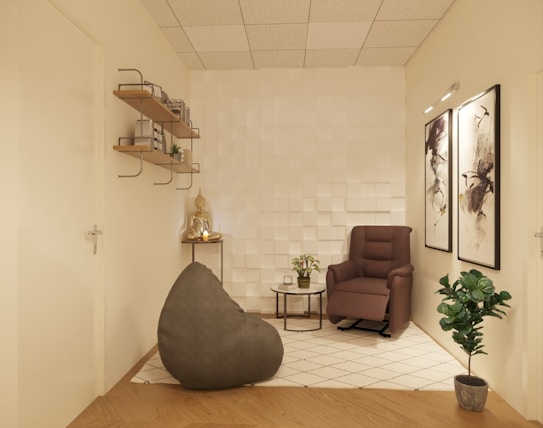 A cozy, minimalist room with neutral tones featuring a comfortable armchair, a bean bag, a small side table with plants, and decorative artwork on the walls. The shelves on the left hold various books and small decor items. The room has a modern white textured wall and wooden flooring with a geometric pattern rug.
