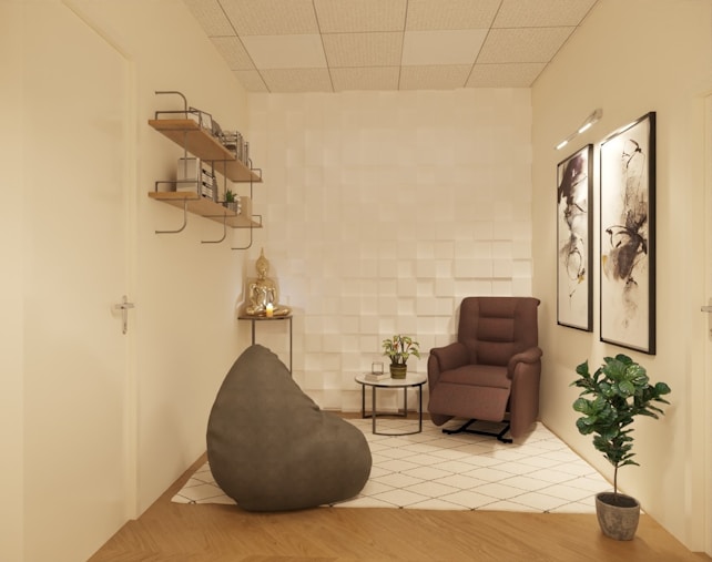 A cozy, minimalist room with neutral tones featuring a comfortable armchair, a bean bag, a small side table with plants, and decorative artwork on the walls. The shelves on the left hold various books and small decor items. The room has a modern white textured wall and wooden flooring with a geometric pattern rug.