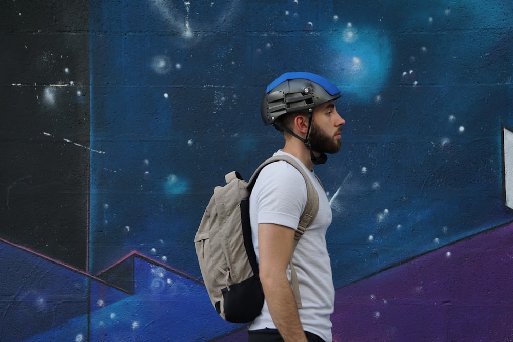 a man with a backpack and helmet walking by a wall