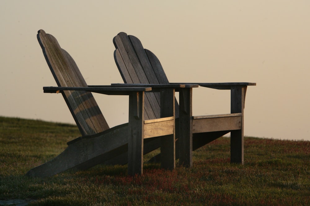 a couple of wooden chairs sitting on top of a lush green field