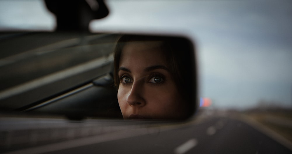 a woman's reflection in the side view mirror of a car