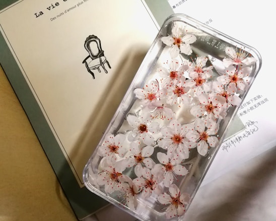 Soft pastel phone cases arranged artfully on a light wooden table with delicate flowers nearby.