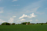 A peaceful rural farmhouse surrounded by green fields under a bright blue sky.