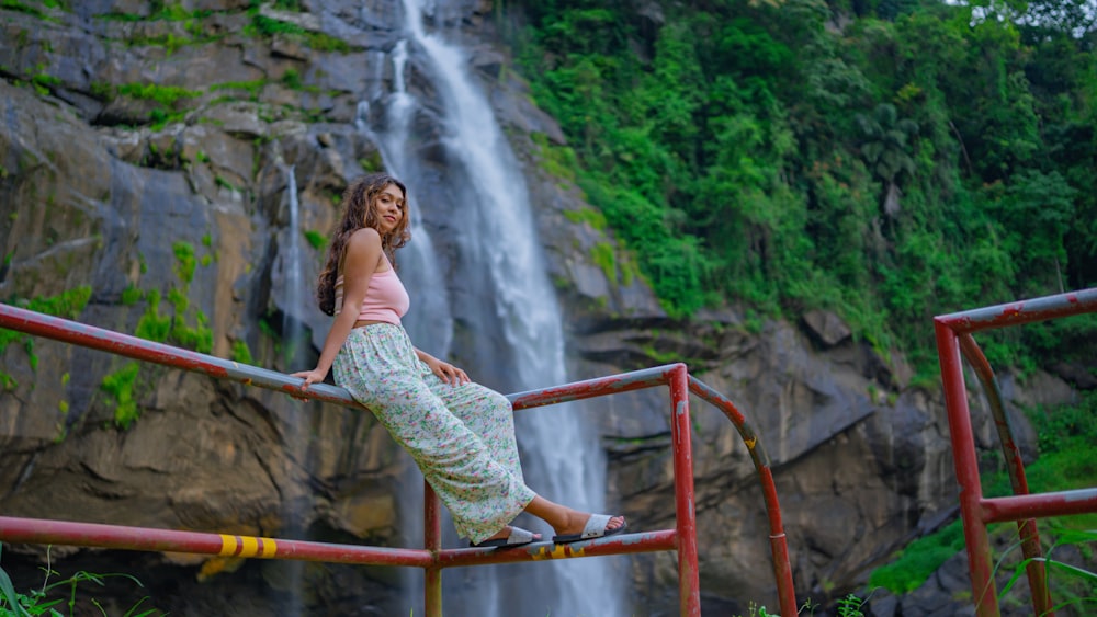 a woman standing on a railing in front of a waterfall