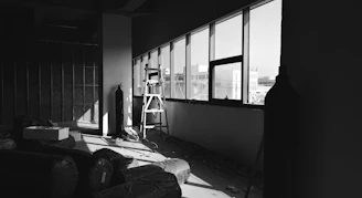 A sleek, dark steel-toned office space with a large window overlooking a vast warehouse filled with steel beams and pipes.