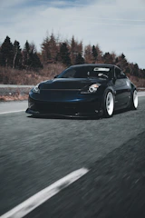 A sleek black sports car captured in motion on a winding mountain road at dusk.