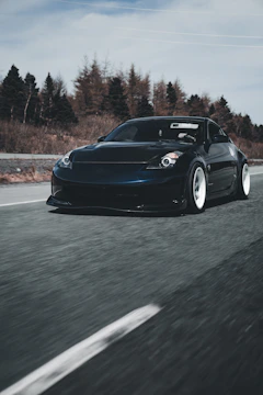 A sleek black sports car captured in motion on a winding mountain road at dusk.