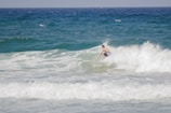 A surfer catching a wave on a golden beach in Fiji under a bright blue sky.