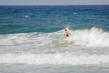 A surfer catching a wave on Taghazout beach under a bright blue sky.
