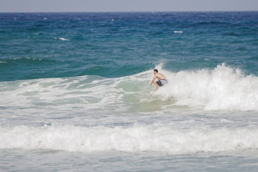 Surfer catching a wave on the sunny Agadir beach with clear blue sky.