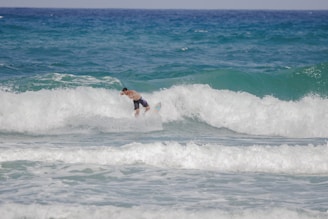 A surfer navigates through the crashing waves of the ocean, surrounded by frothy white water and deep blue sea. The scene conveys the energy and thrill of mastering the waves.