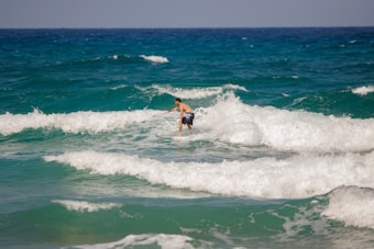 A person is surfing on ocean waves, showcasing a sense of adventure and skill. The sea is vibrant with varying shades of blue and green, while the sky is clear, suggesting a sunny day.