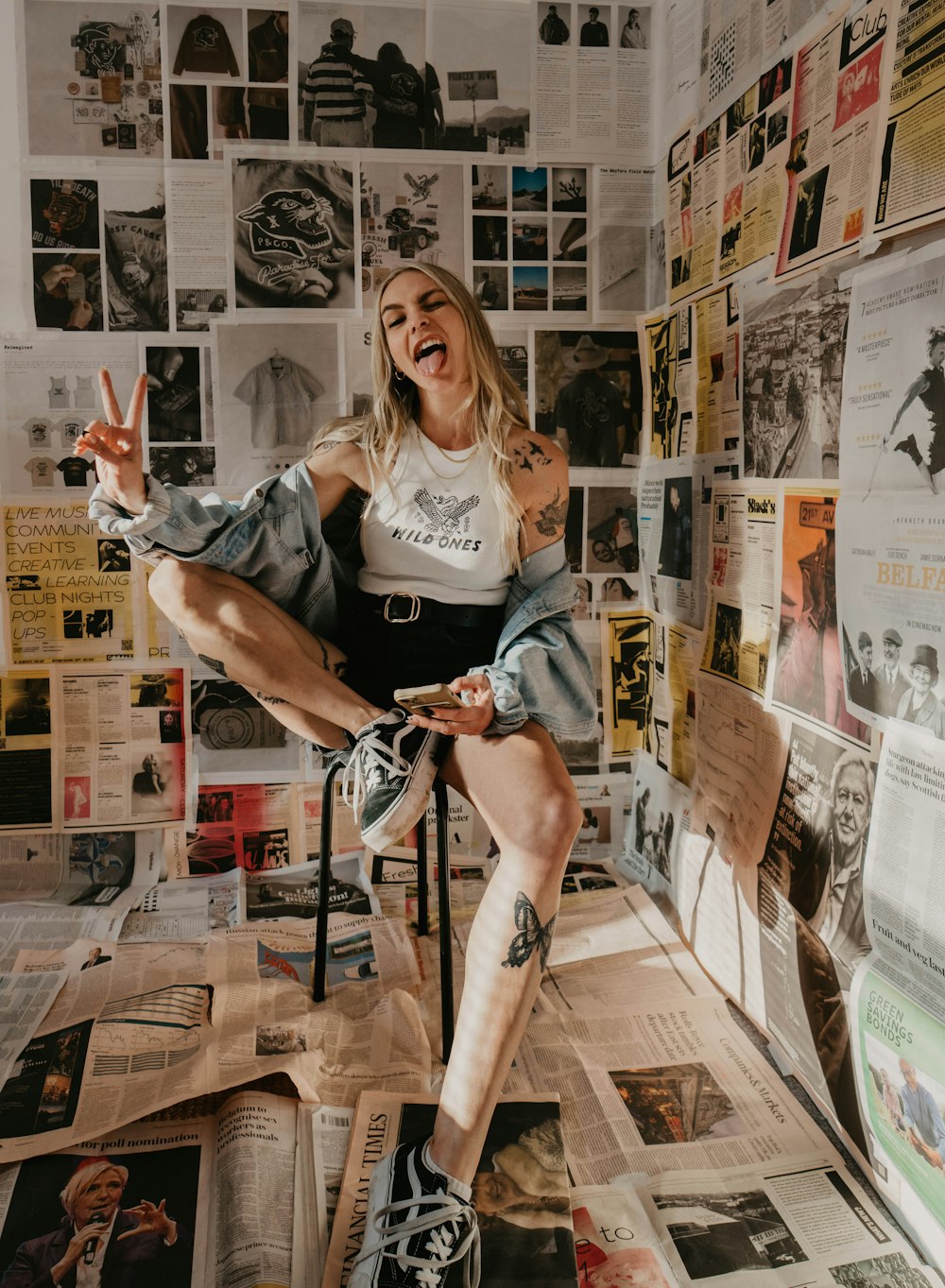 a woman sitting on top of a chair in front of a wall covered with posters