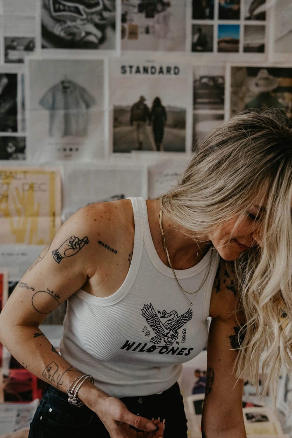 a woman in a white tank top standing in front of a wall covered with pictures