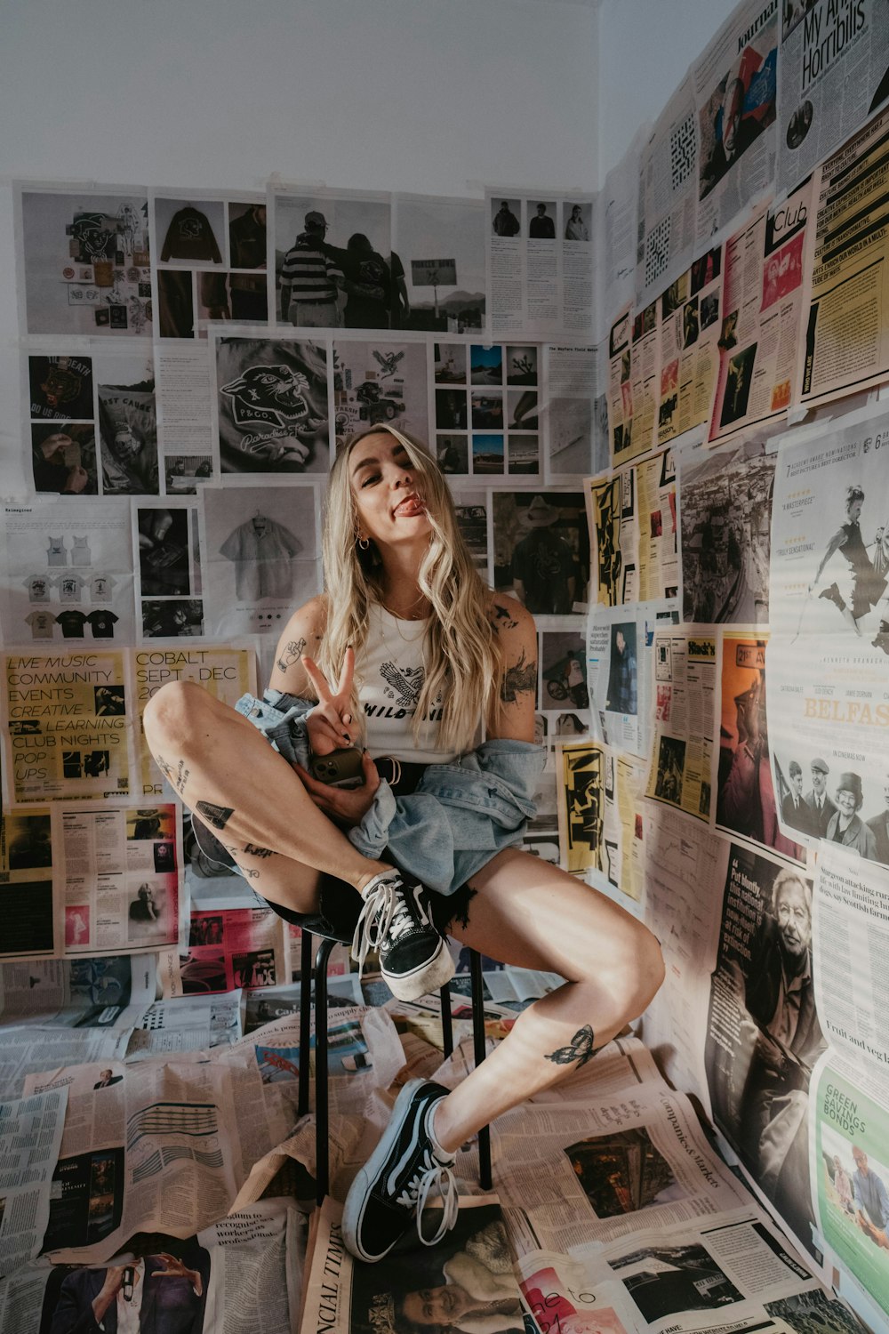 신문으로 덮인 벽 앞 의자에 앉아 있는 여자