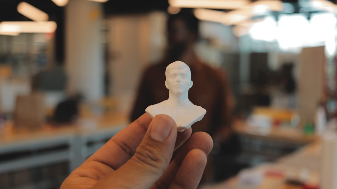 a person is holding a small white statue, The subject holds a 3D-printed face in their hand.