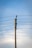 A concrete utility pole supports several electrical wires extending horizontally against a clear blue sky. The wires are evenly spaced and attached using insulators on the pole.