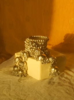 A stack of ornate silver bangles and jhumka earrings styled on a beige box, casting reflections and shadows on the soft fabric below, against a warm golden backdrop.