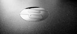 A close-up shot of a textured surface featuring a shiny, circular logo with stylized letters in the center. The logo appears to contrast with the matte surface, creating a sleek and modern aesthetic.