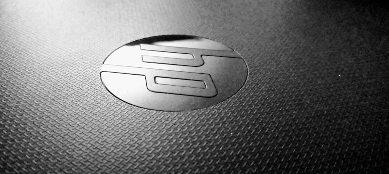 A close-up shot of a textured surface featuring a shiny, circular logo with stylized letters in the center. The logo appears to contrast with the matte surface, creating a sleek and modern aesthetic.