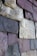 A close-up view of a textured stone wall composed of irregularly shaped, overlapping slabs. The stones have a mix of colors, including shades of gray, purples, and browns, highlighting the rough surface and natural grain of each piece.