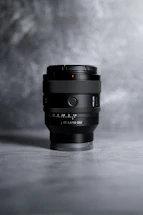 A moody, dark-toned photo of a camera lens resting on a sleek black surface, hinting at creative focus.